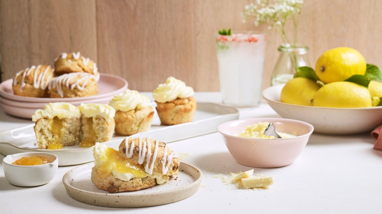 A collection desserts on a table, including lemon and white chocolate scones and fresh lemons
